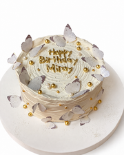 Beyaz arka planda beyaz altın kelebekli Happy Birthday mesajlı pasta